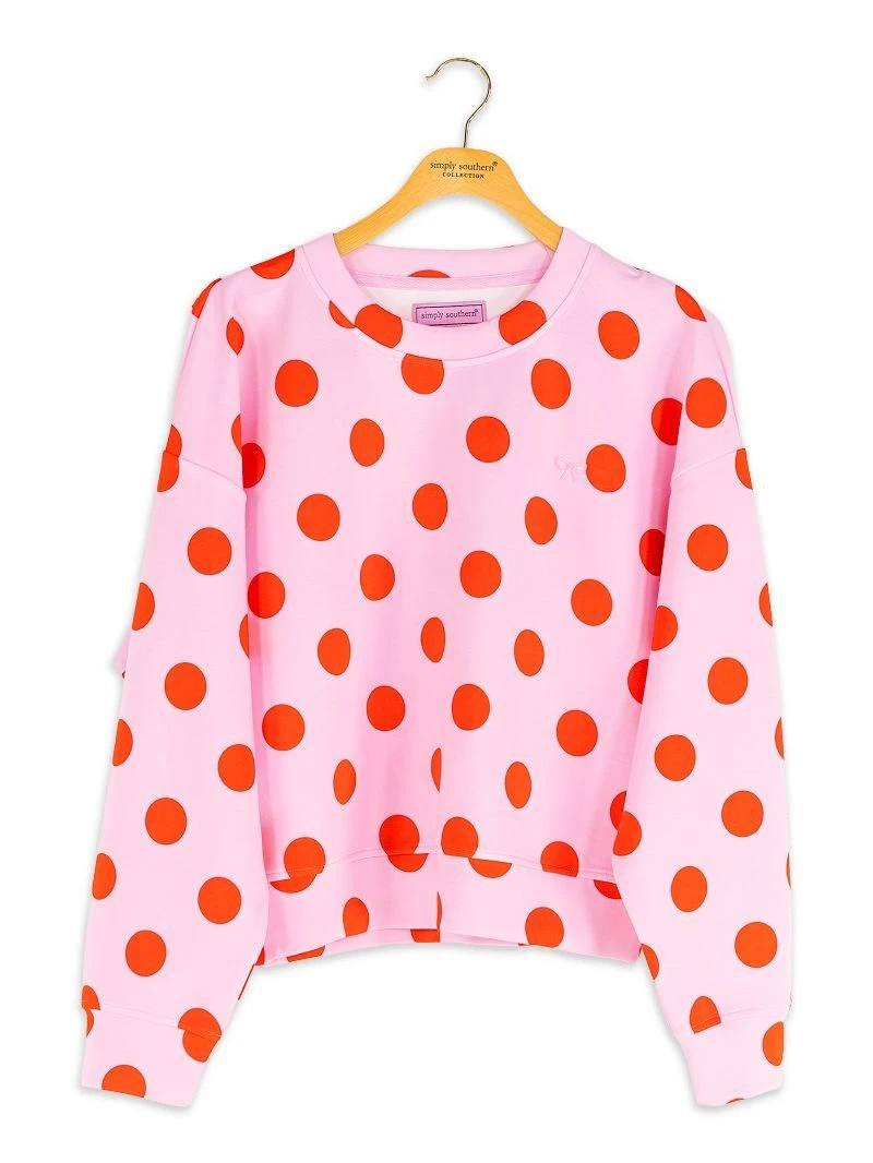 A pink long-sleeve sweatshirt with a bold orange polka dot pattern, hanging on a wooden hanger against a plain white background.