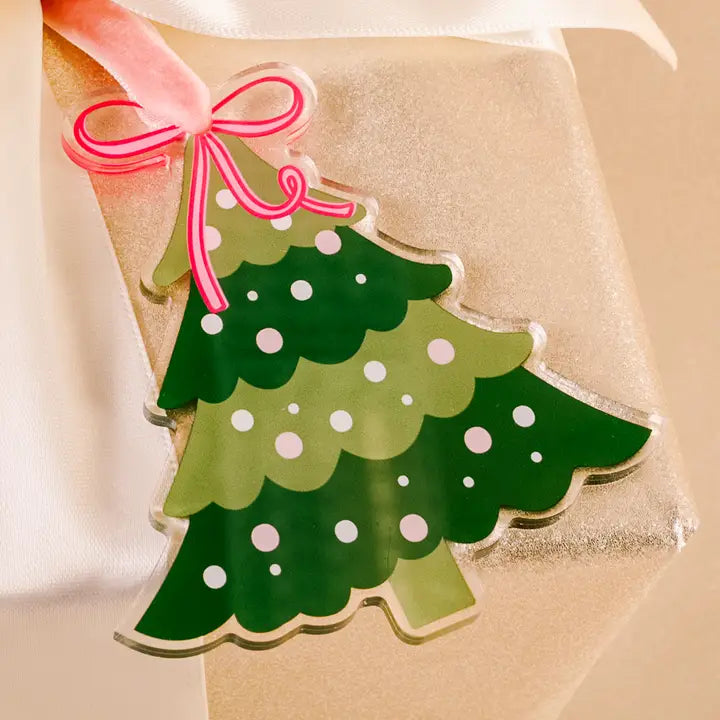 Green Christmas tree-shaped gift tag with pink bow on beige background