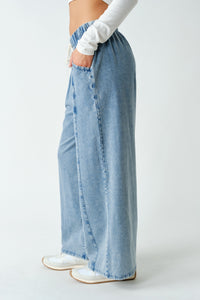 A person wearing light-wash wide-leg denim pants with side pockets, paired with a white long-sleeve top and white sneakers, shown from the waist down against a plain light gray studio background.