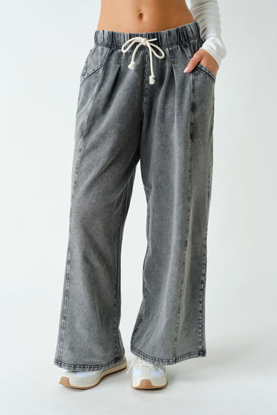 A person wearing wide-leg gray denim pants with an elastic waistband and white drawstring, paired with white sneakers against a plain light gray studio background.