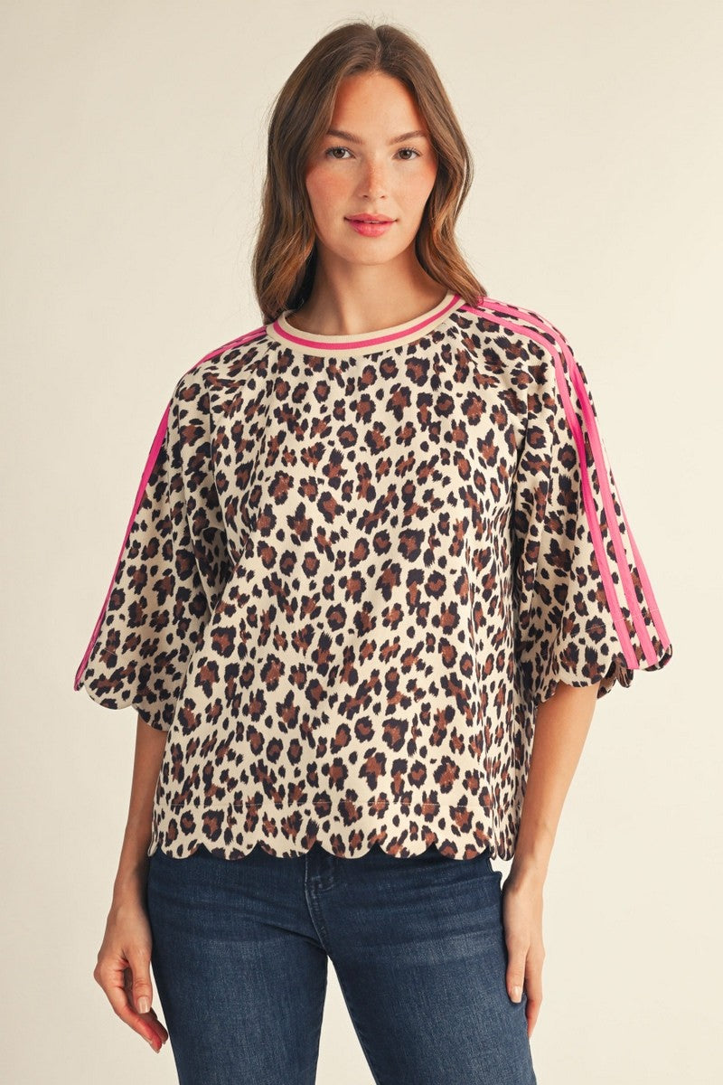 A woman wearing a leopard print top with pink trim and pink stripes on the sleeves, paired with blue jeans, against a plain beige background.
