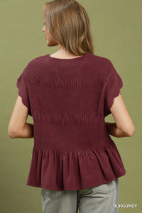 Woman wearing a burgundy top with fringes on a green background