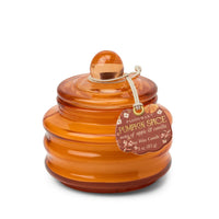 An amber glass jar candle with a matching lid and a hanging tag that reads 'Paddywax Pumpkin Spice notes of Apple & vanilla'.