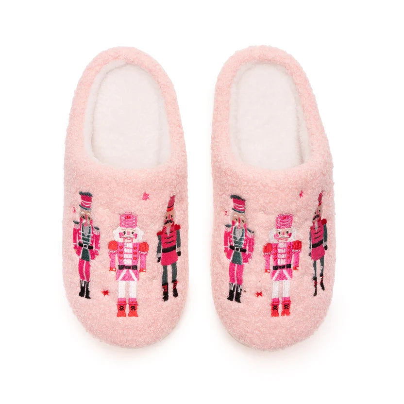 A pair of fuzzy light pink slip-on slippers decorated with colorful nutcracker soldier illustrations, shown against a plain white background.