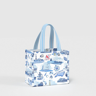 A small tote bag with blue and white striped handles, featuring a blue illustrated North Carolina landscape print on a white background, photographed against a light gray studio backdrop.