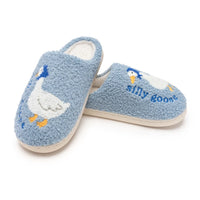 A pair of light blue fuzzy slip-on slippers featuring embroidered white ducks with yellow beaks and feet, and the text 'silly goos' on the side, shown on a white background.