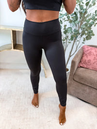 Person wearing black leggings standing in a room with a couch and plant.