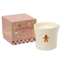 A Paddywax Gingerbread scented soy wax candle in a white ceramic holder with a gingerbread figure decoration, shown next to its pink illustrated packaging box.