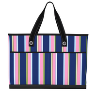 A striped tote bag with vertical pink, navy, white, and lime green stripes, featuring black shoulder straps with white stitching and silver metal grommets.
