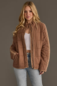 Woman wearing a brown quilted jacket against a plain background
