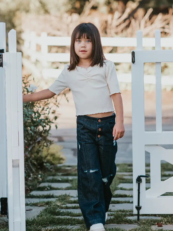 Child standing in front of a white picket fence with a blurred natural background