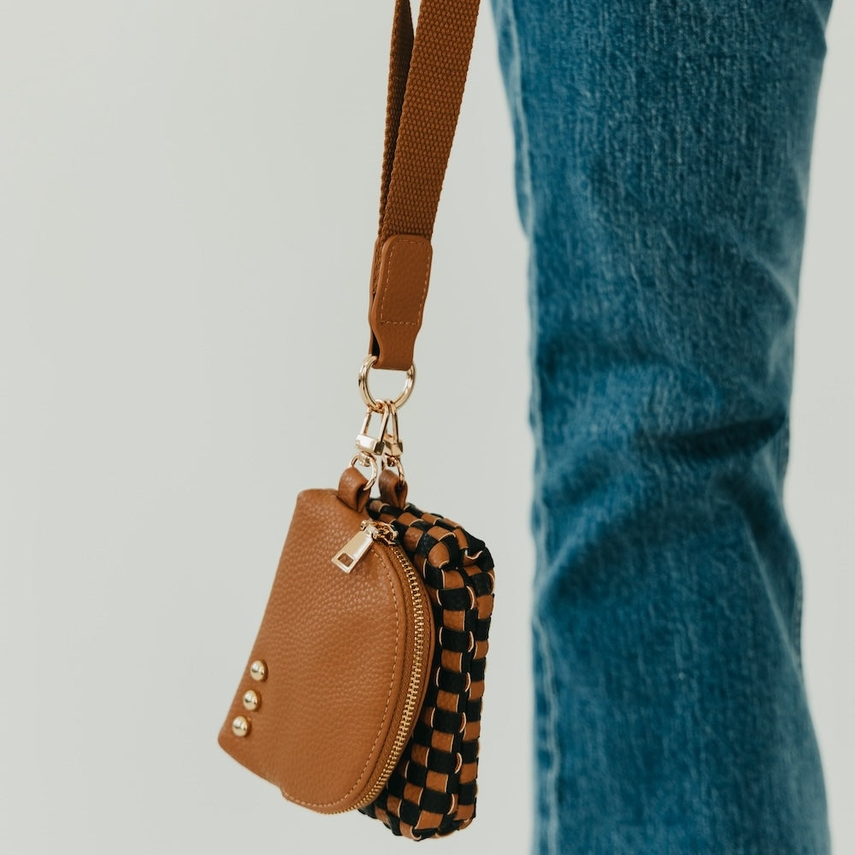 Brown leather pouch with woven design attached to a strap, worn over blue jeans.