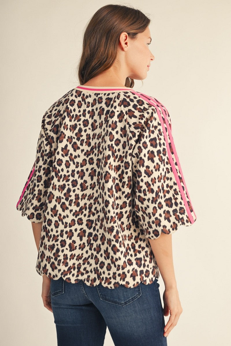 A woman shown from the back wearing a leopard print blouse with pink trim and flared sleeves, paired with blue jeans, against a plain beige studio background.