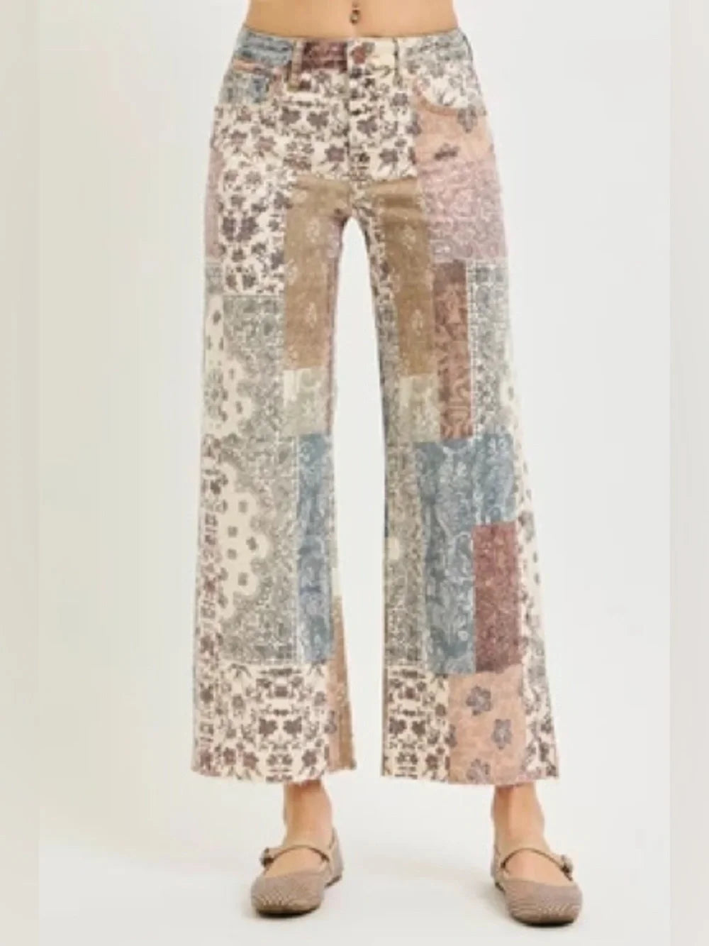 A person wearing patchwork wide-leg cropped pants with a multicolor floral and abstract print in beige, blue, pink, and brown tones, paired with flat tan shoes against a plain light background.