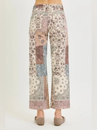 A pair of cropped wide-leg pants with a multicolor patchwork pattern of floral and paisley motifs in beige, pink, blue, and brown, shown on a model from the back against a plain light background.